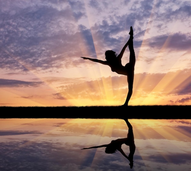 Concepto de meditación y relajación. Silueta de una niña practicando yoga al atardecer y reflejo en el agua