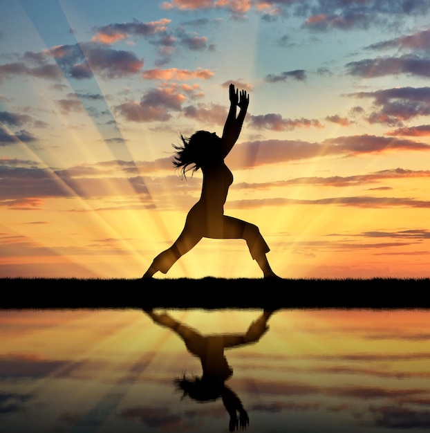 Concepto de meditación y relajación. Silueta de una niña practicando yoga al atardecer y reflejo en el agua