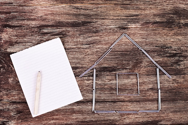 Concepto de mejoras para el hogar: casa modelo de madera en una mesa de trabajo con herramientas y cuaderno de espiral vacío