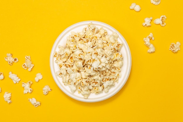 Concepto de merienda Palomitas de maíz dulces en plato blanco y cayendo sobre fondo amarillo