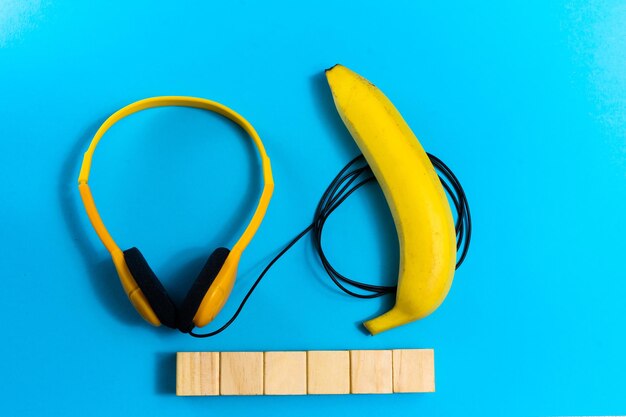 Concepto de minimalismo plano, escucha música. Auriculares, banana sobre fondo azul. Vista superior