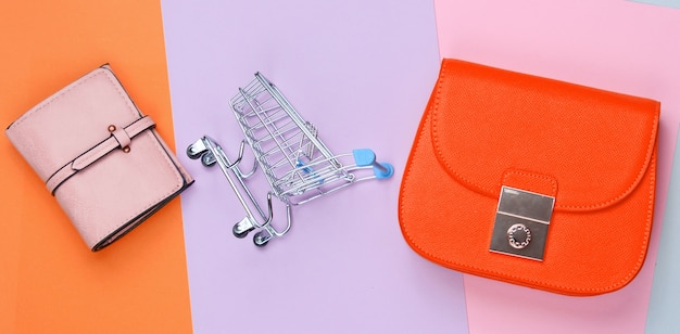 Concepto minimalista adicto a las compras. Bolso, bolso, mini carrito de la compra sobre fondo pastel. Vista superior