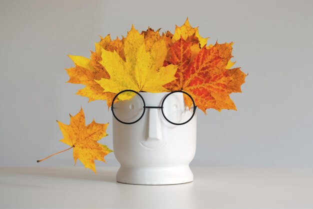 Foto concepto minimalista de otoño hojas de arce en jarrón con cara