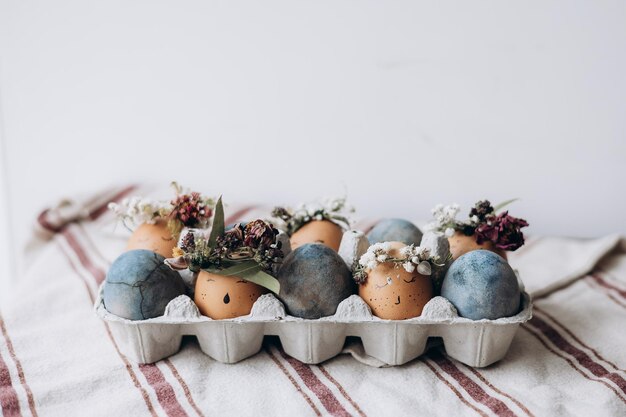 Concepto mínimo de celebración de Pascua huevos de gallina teñidos con divertidos emoticonos en paquete de cartón Huevos de Pascua de color pastel en caja de huevos sobre fondo claro con espacio de copia