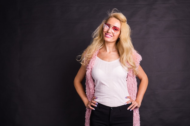 Concepto de moda y belleza - Hermosa mujer rubia vestida con camisa blanca y rebeca rosa sobre fondo oscuro con espacio de copia