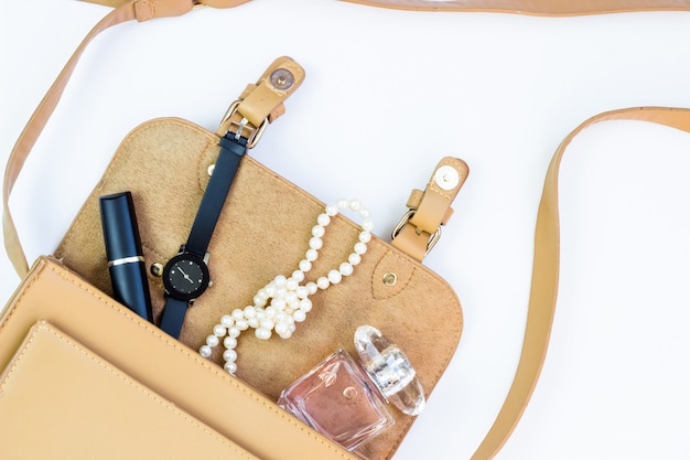 Foto concepto de moda: bolso de mujer con cosméticos, accesorios y un teléfono inteligente en blanco