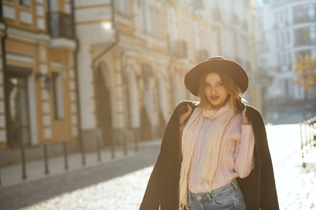 Concepto de moda de la calle: elegante joven con sombrero y suéter posando con la luz del sol. Espacio para texto