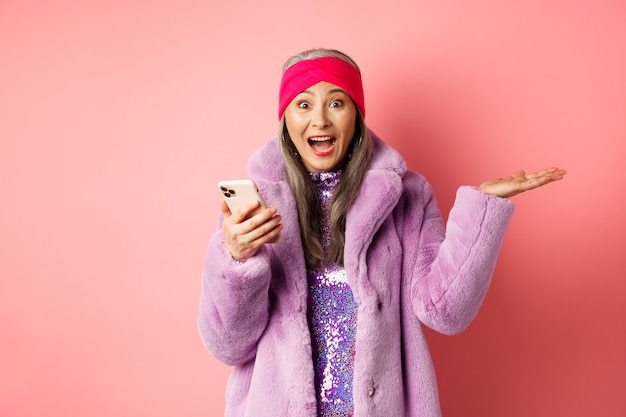 Concepto de moda y compras en línea. Mujer mirando impresionante oferta promocional en smartphone, grito de alegría, mirando con cara sorprendida y feliz en rosa.