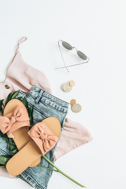 Foto concepto de moda femenina con flor de peonía blanca, zapatillas, gafas de sol, pendientes, pantalones cortos, camiseta sobre superficie blanca