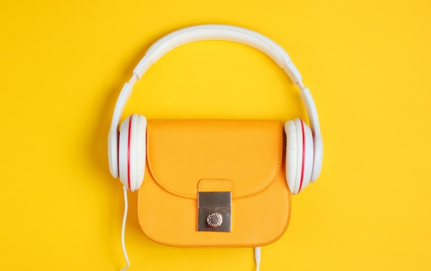 Concepto de moda minimalista. Bolso de cuero amarillo de moda con auriculares sobre un fondo amarillo. Vista superior