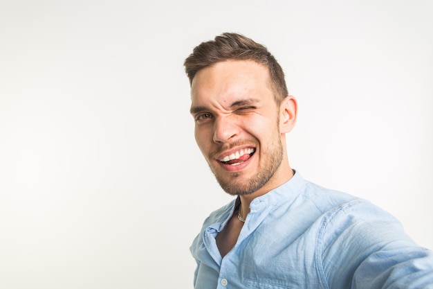 Concepto de moda y personas - hombre guapo hace una foto selfie y sonriendo sobre fondo blanco.