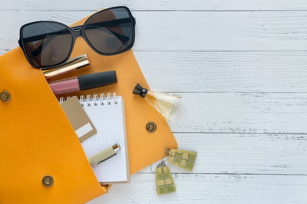 Concepto de la moda Productos cosméticos, gafas de sol, cuaderno y bolso naranja.