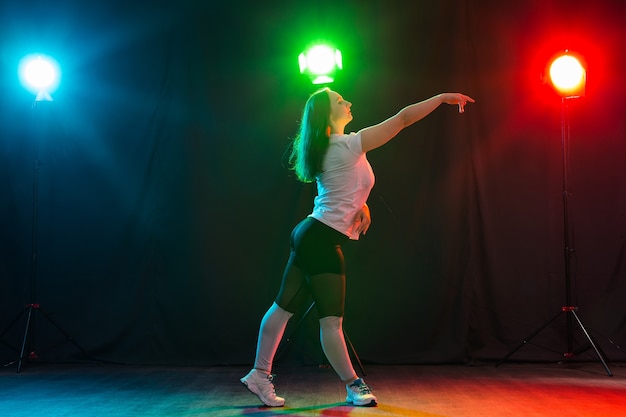 Concepto moderno de danza, deporte y personas - mujer joven bailando jazz funk en la oscuridad bajo una luz colorida.