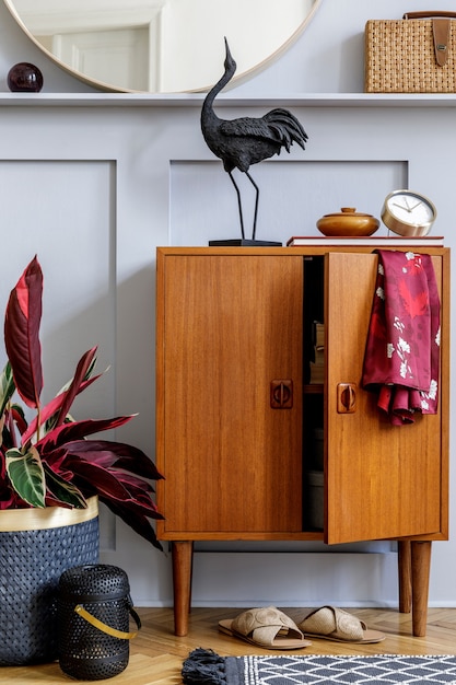 Concepto moderno de decoración casera con inodoro de madera de diseño, espejo redondo, estante, reloj, planta, decoración de ratán, libro, linternas y elegantes accesorios personales en la elegante sala de estar.