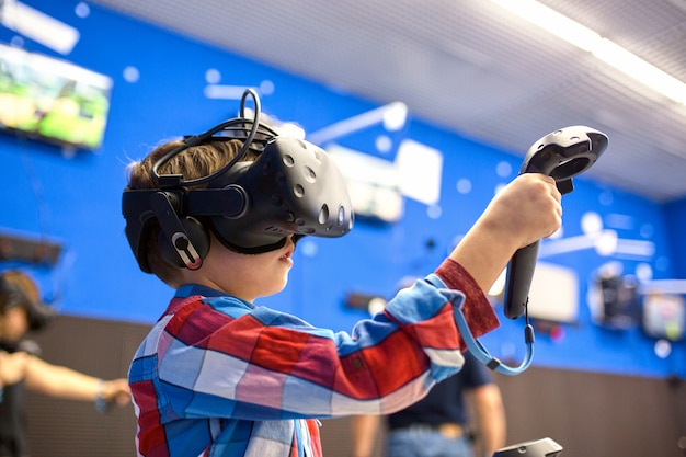 Concepto moderno de tecnología, juegos y personas: niño con casco de realidad virtual o gafas 3D jugando videojuegos en el centro de juegos