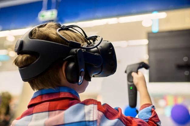 Foto concepto moderno de tecnología, juegos y personas: niño con casco de realidad virtual o gafas 3d jugando videojuegos en el centro de juegos
