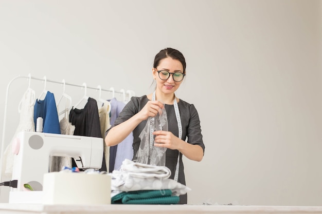 Concepto de modista, sastre, moda y sala de exposición - Retrato de una talentosa modista que trabaja con textiles para coser ropa.