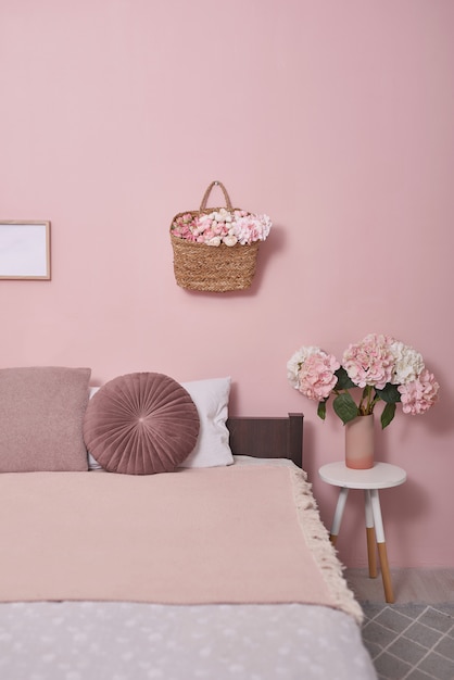 Concepto de muebles de dormitorio interior. Acogedor rincón rosa dormitorio. Acogedor y femenino dormitorio con cama rosa, cojines decorativos y plantas en un taburete de madera.