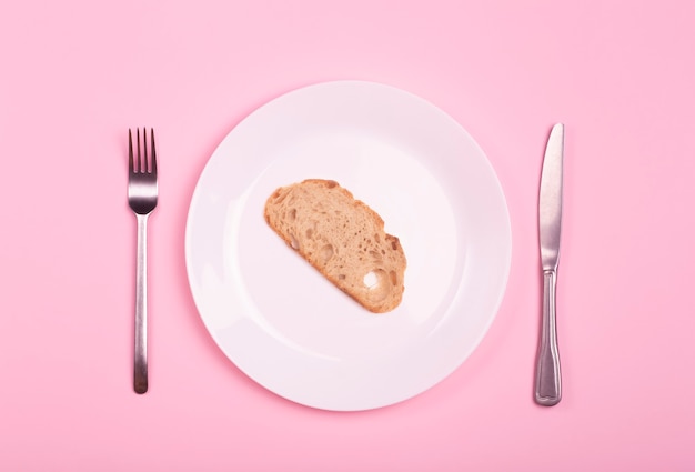 Concepto mundial de hambre y pobreza. Un trozo de pan en un plato vacío sobre una mesa rosa.