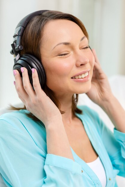 concepto de música, entretenimiento y felicidad - mujer feliz y sonriente con auriculares en casa