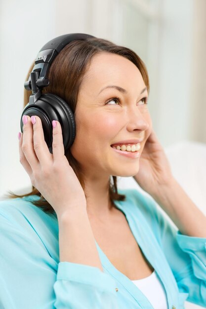 concepto de música, entretenimiento y felicidad - mujer feliz y sonriente con auriculares en casa