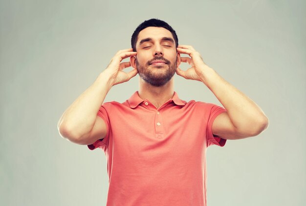 concepto de música, gesto y gente - hombre feliz y sonriente escuchando música con auriculares imaginarios sobre un fondo gris