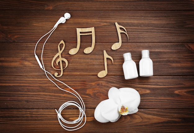 Concepto de música Spa Notas auriculares orquídeas y botellas de crema sobre fondo de madera