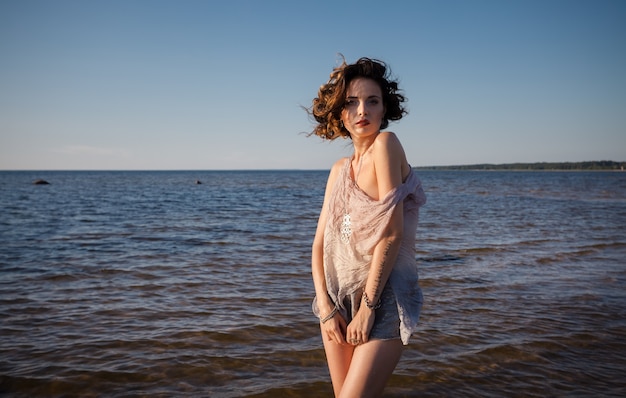 Concepto de naturaleza, belleza, juventud y estilo de vida saludable. Mujer semidesnuda joven atractiva en un traje de neopreno posando sobre el fondo del mar. Luz del atardecer con sombras profundas y cambio de color.