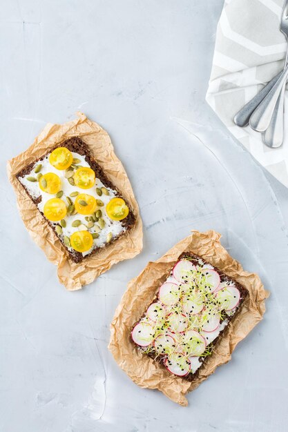 Concepto de naturaleza muerta de alimentos y bebidas Variedad de sándwiches hechos a mano con tomates de rábano con queso crema y micro brotes verdes para la mesa del almuerzo Vista superior de fondo plano