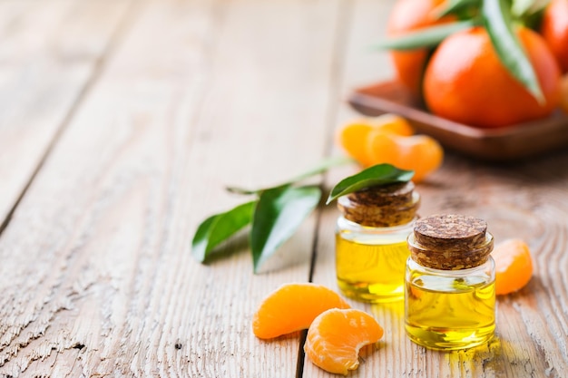 Concepto de naturaleza muerta de salud y belleza Aceite de clementina de mandarina esencial orgánico en un frasco de vidrio pequeño con hojas verdes y fruta naranja en una mesa de madera rústica Fondo de espacio de copia