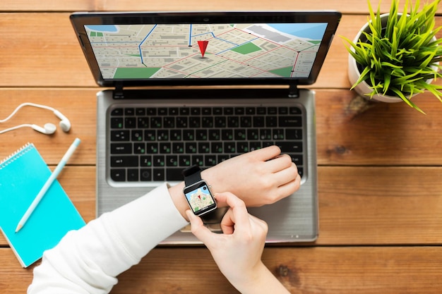 Foto concepto de navegación, ubicación, negocios, personas y tecnología - cierre de una mujer con un reloj inteligente y una computadora portátil en una mesa de madera con un mapa del navegador gps en las pantallas