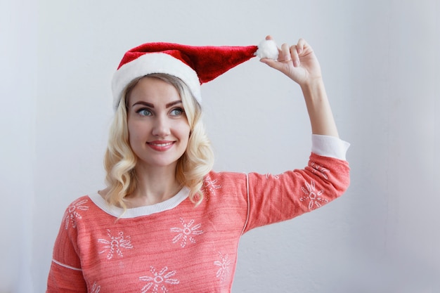 Concepto de Navidad y año nuevo. Hermosa joven rubia en una gorra de año nuevo sonriendo. Contra una pared blanca