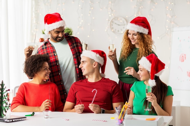 Foto concepto de navidad, celebración y fiestas - equipo feliz en sombreros de santa con chispas y vino espumoso no alcohólico en la fiesta de la oficina corporativa