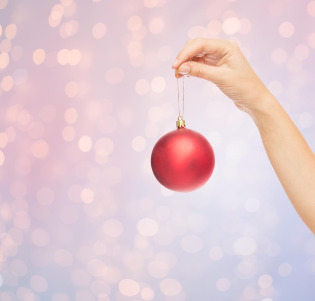 concepto de navidad, decoración, vacaciones y personas - cierre de la mano de una mujer sosteniendo una bola de navidad sobre fondo de luces de cuarzo rosa y serenidad