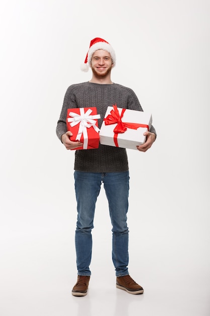 Concepto de Navidad - Feliz joven con barba lleva una gran cantidad de regalos aislados en la pared blanca.