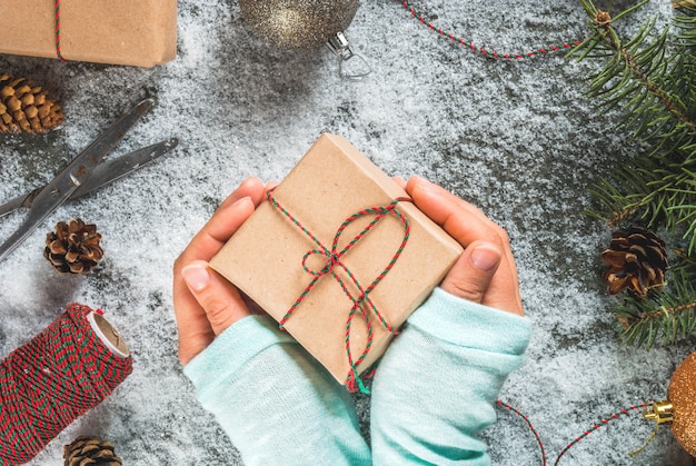 Concepto de Navidad, fondo de mesa con nieve, ramas de árboles de Navidad, niña sostiene en manos regalos o regalos, piñas y decoración
