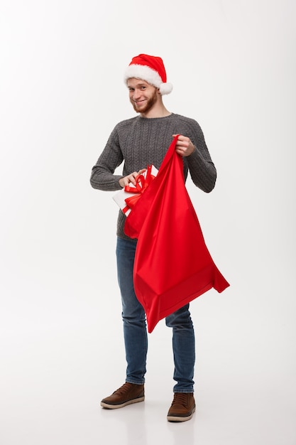 Concepto de la Navidad - El hombre feliz joven de la barba excita con el presente grande en bolso de santa.