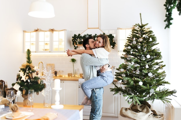 Concepto de Navidad, hombre y mujer enamorados se abrazan y besan en la cocina luminosa decorada en casa