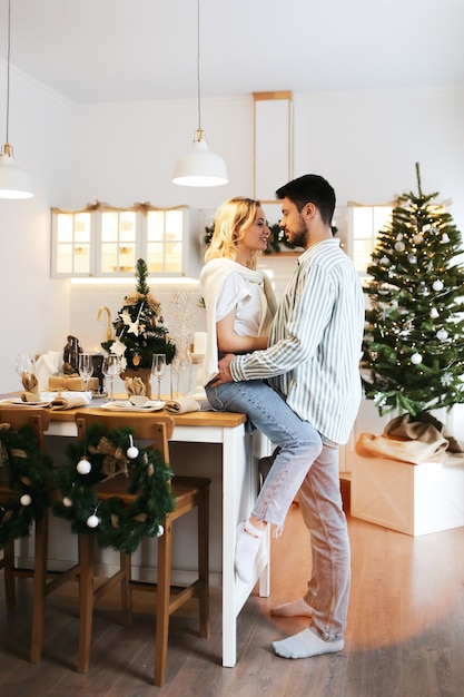 Concepto de Navidad, hombre y mujer enamorados se abrazan y besan en la cocina luminosa decorada en casa