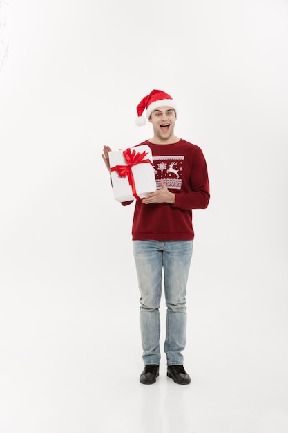 Concepto de Navidad - joven apuesto de cuerpo entero en suéter con regalo de Navidad blanco.