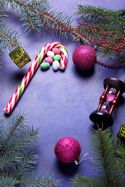 Concepto de Navidad juguetes de Navidad reloj de arena bastón de caramelo ramas de árboles de Navidad sobre un fondo púrpura Primer plano