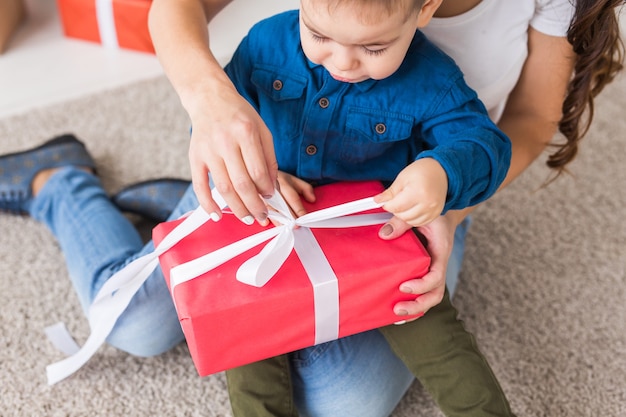 Concepto de Navidad, monoparental y vacaciones - Primer plano de niño lindo con regalo de Navidad para su madre en el hogar.