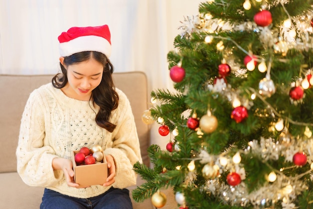 Concepto de navidad Mujer asiática joven en sombrero de santa sosteniendo caja de bola de navidad para decoración