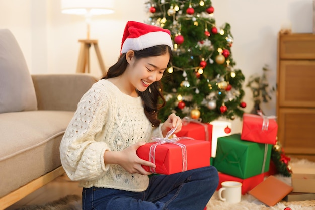 Concepto de Navidad Mujer asiática sentada en la sala de estar decorada con Navidad y regalo de Navidad abierto