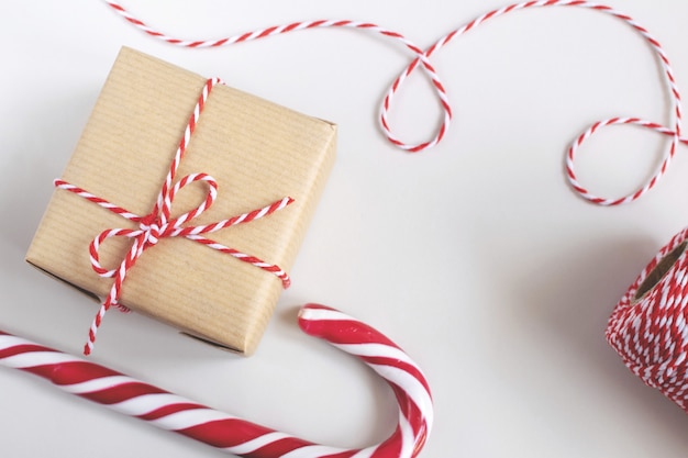 Concepto de Navidad o Año Nuevo: caja presente en papel artesanal, bastones de caramelo, cordón trenzado rojo y blanco.