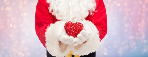 concepto de navidad, vacaciones, amor, caridad y personas - cierre de santa claus con decoración en forma de corazón sobre cuarzo rosa y fondo de luces de serenidad