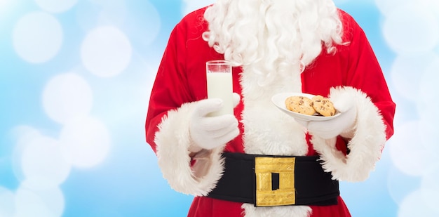 concepto de navidad, vacaciones, comida, bebida y personas -cierre de santa claus con un vaso de leche y galletas sobre fondo de luces azules