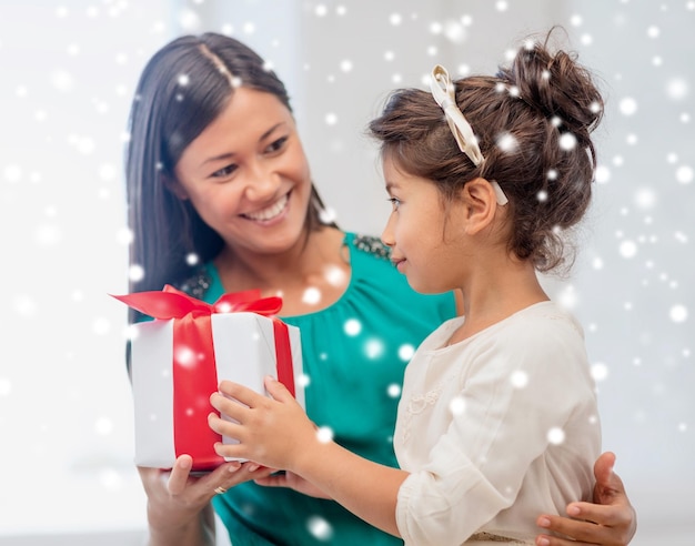 concepto de navidad, vacaciones, familia y personas - madre feliz y niña con caja de regalo en casa