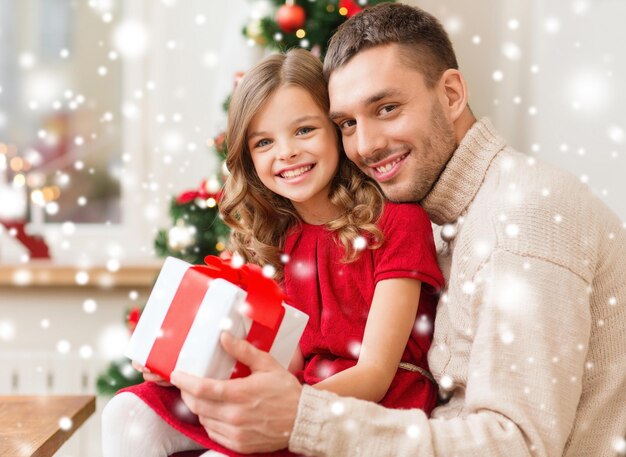 concepto de navidad, vacaciones, familia y personas - padre e hija sonrientes sosteniendo una caja de regalo y abrazándose en casa