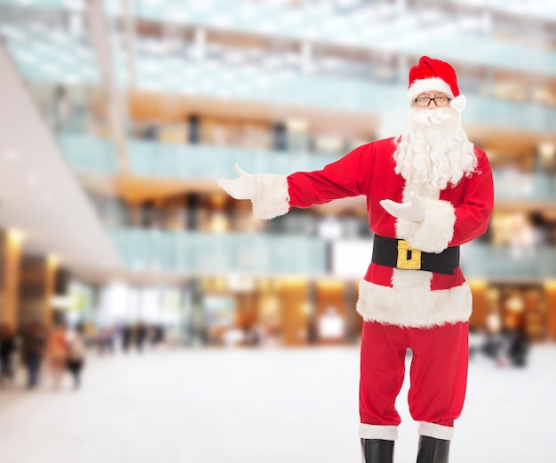 concepto de navidad, vacaciones, gestos y personas - hombre disfrazado de santa claus sobre el fondo del centro comercial